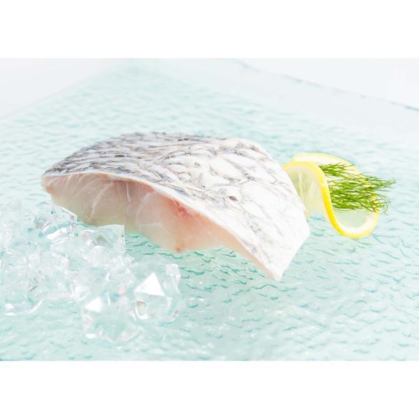 Barramundi fish slice with pale striated flesh, lemon wedge and green herb garnish