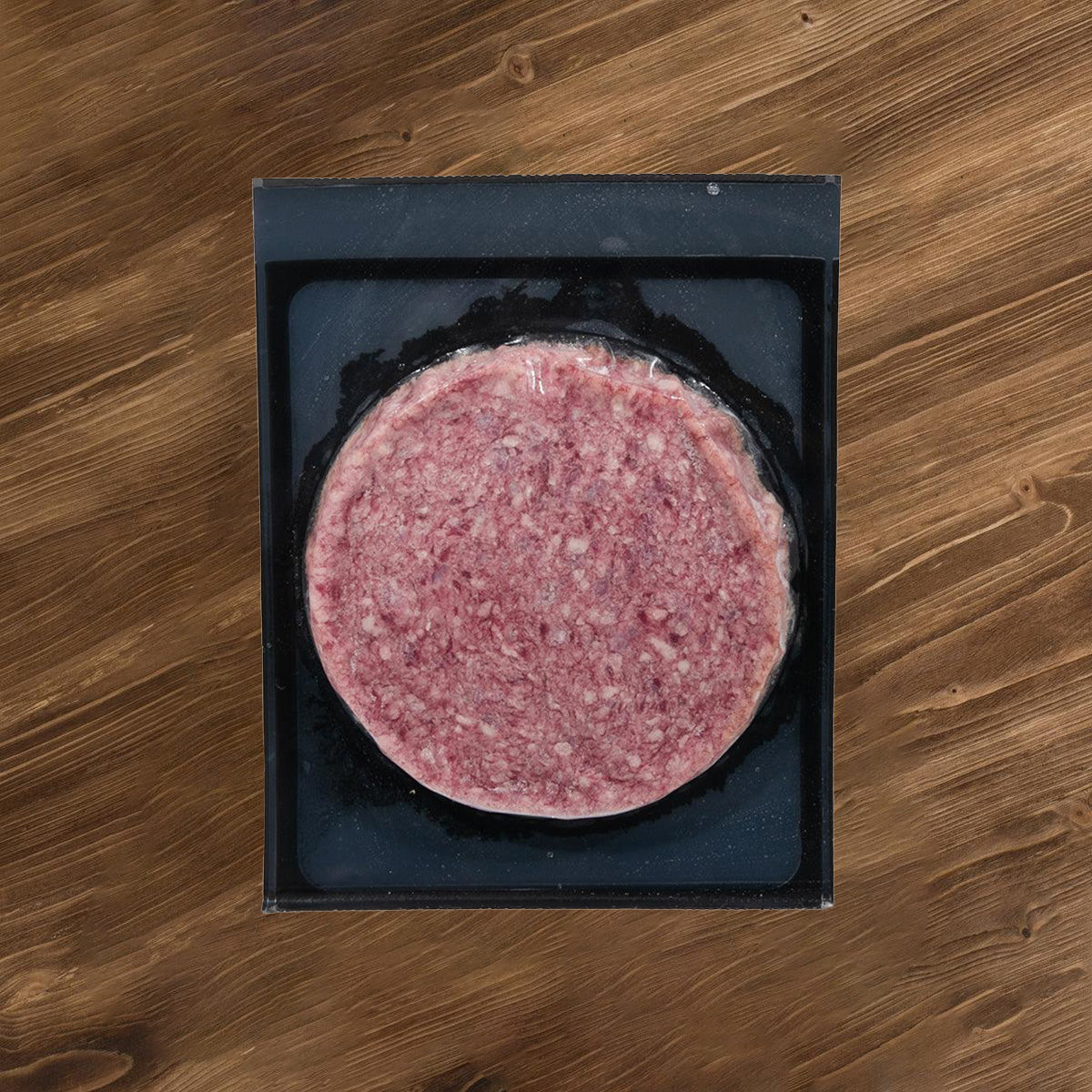 Frozen beef burger patty in black tray, round pink mince