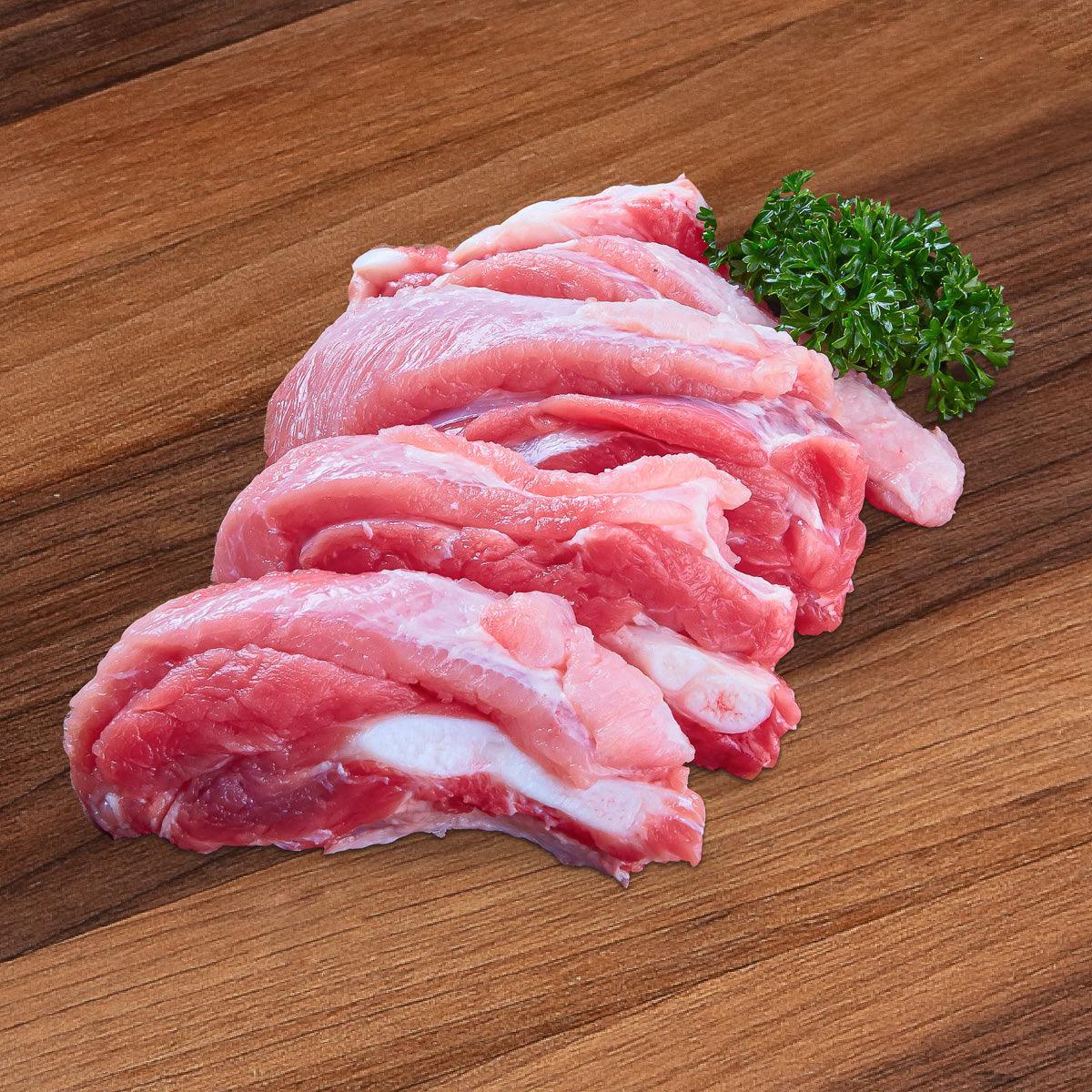 Raw organic pork soft bone cuts, pink meat, with small parsley sprig