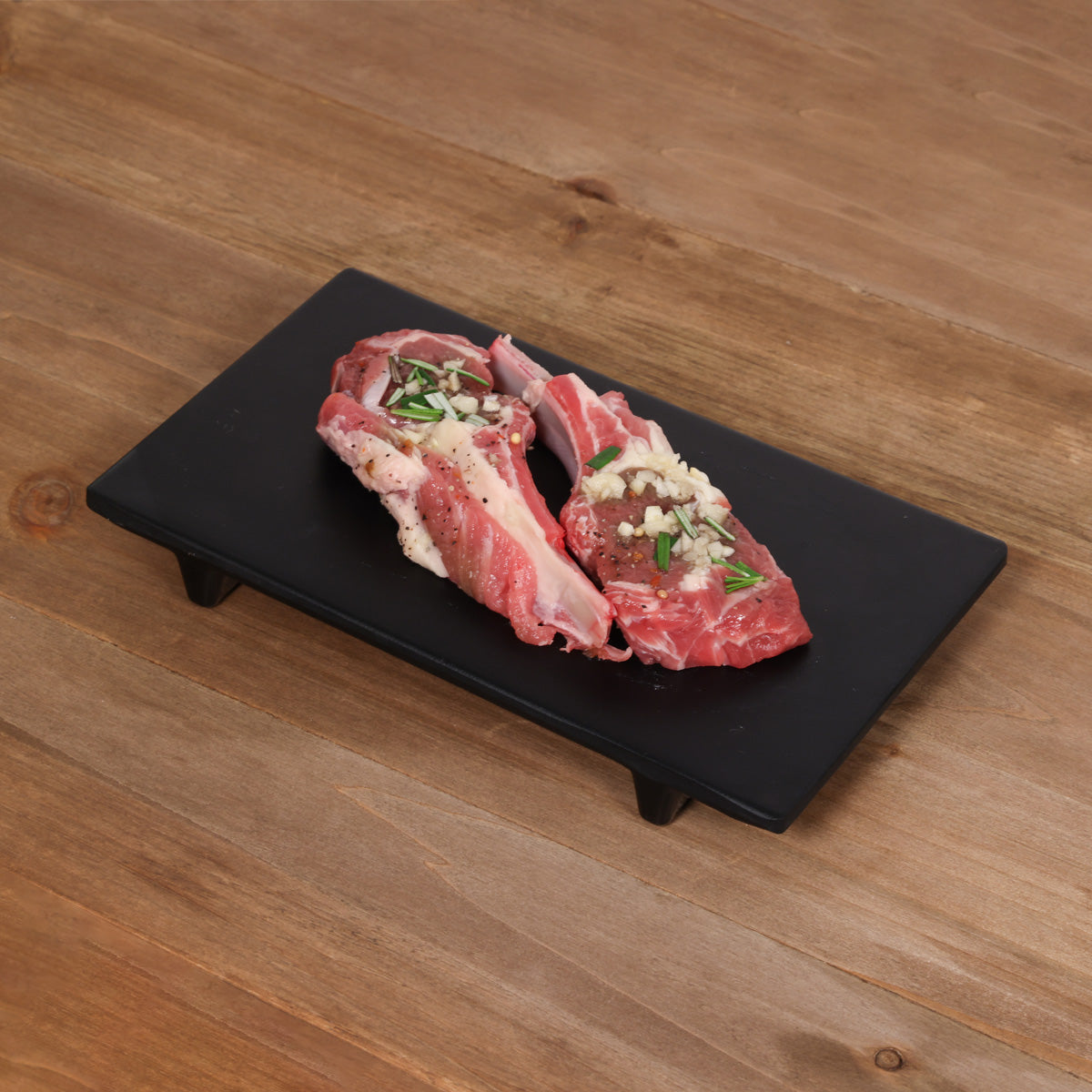 Chilled lamb rack chop with rosemary and garlic, bone-in pieces on a black board