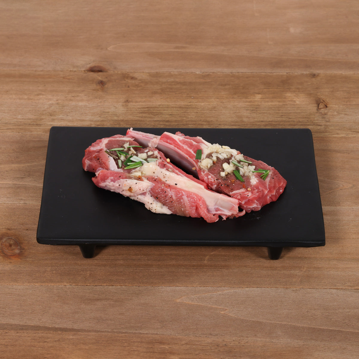 Chilled lamb rack chop with rosemary and garlic, two pieces on a black board