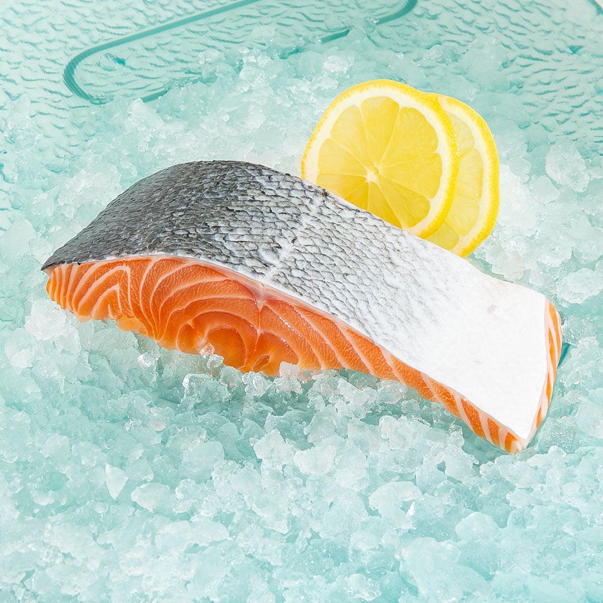 Chilled salmon slice, dark skin side, pink-orange flesh on ice.