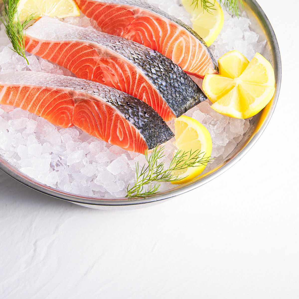 Chilled salmon slices on ice in a bowl with lemon wedges and dill.