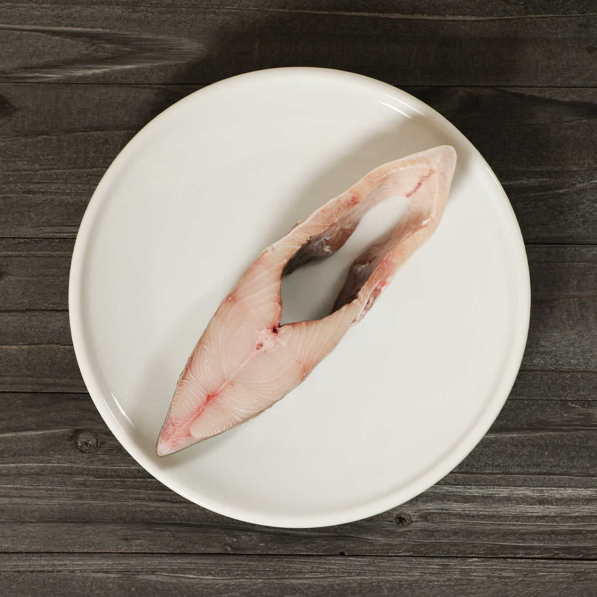 Raw halibut slice on white plate, pink flesh with dark skin patch