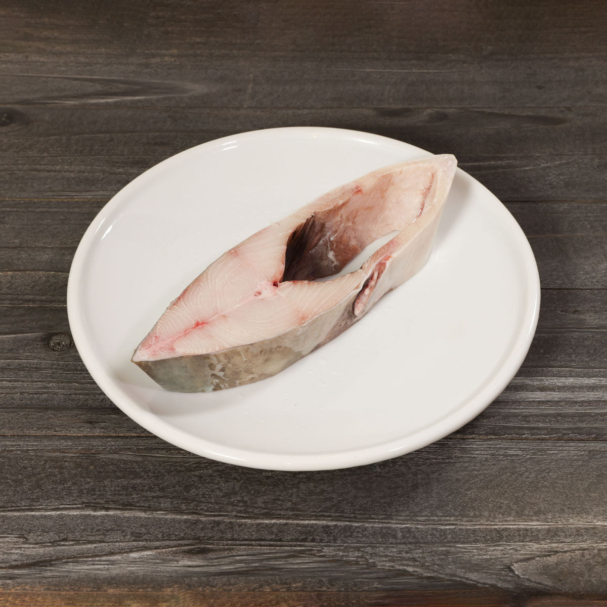 Raw halibut slice on white plate, curved fillet with skin side