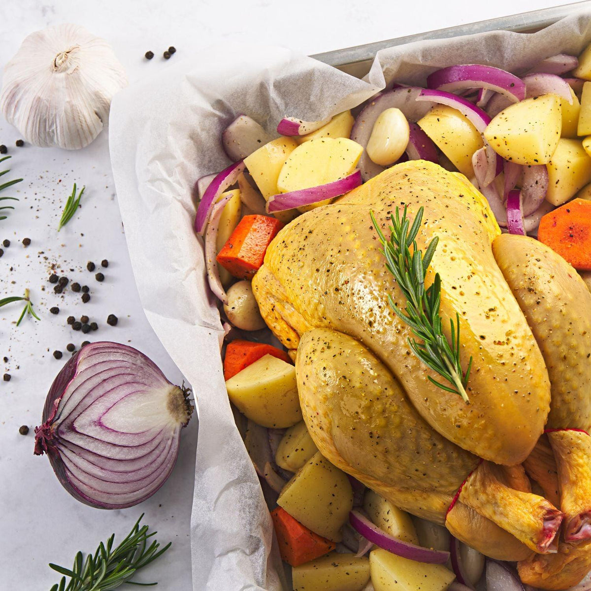 Whole chilled chicken with yellow skin, topped with herbs over assorted vegetables