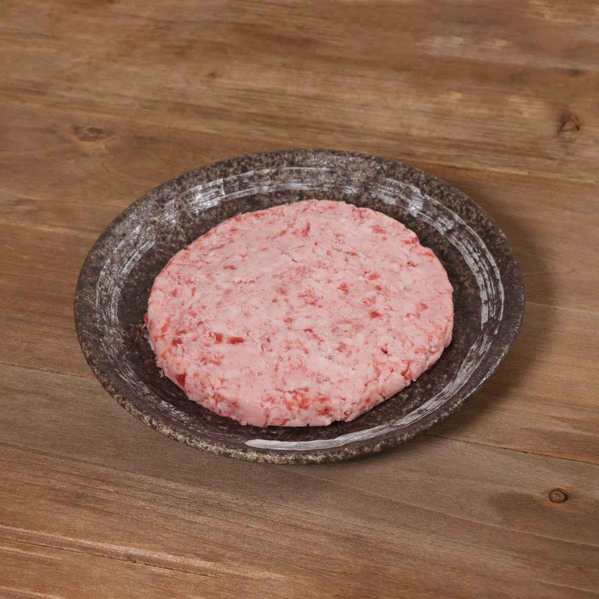 Round pink marbled wagyu beef burger patty in a speckled bowl