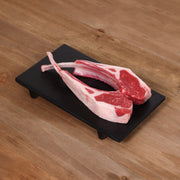 Raw lamb rack chops on black tray, pink meat with red fat
