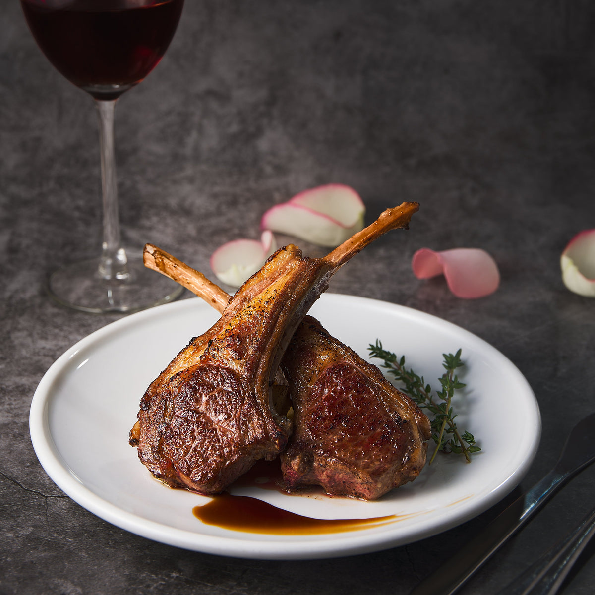 Cooked lamb rack chops on white plate with herbs and pan sauce