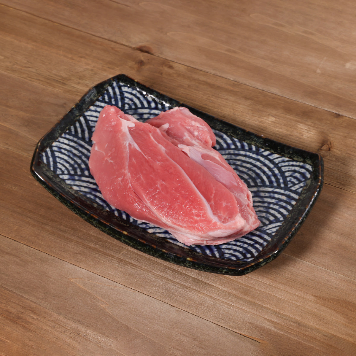 Chilled pork shin pieces on dark patterned tray, visible white fat
