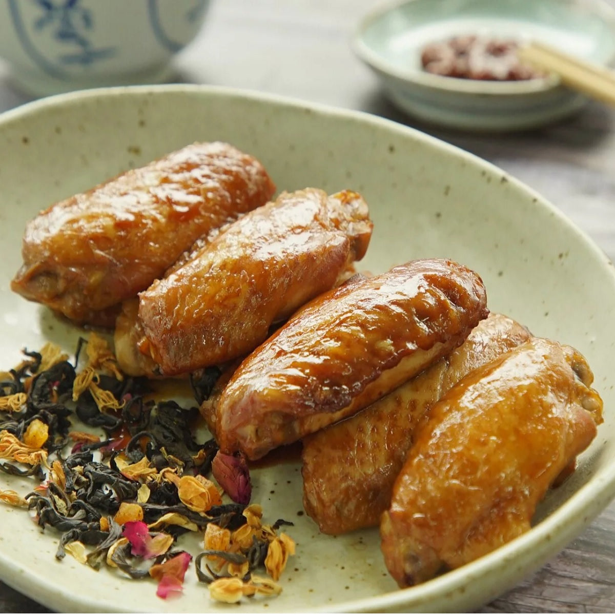 BLUEDROP tea-smoked chicken wings on plate with tea leaves, glossy browned wings