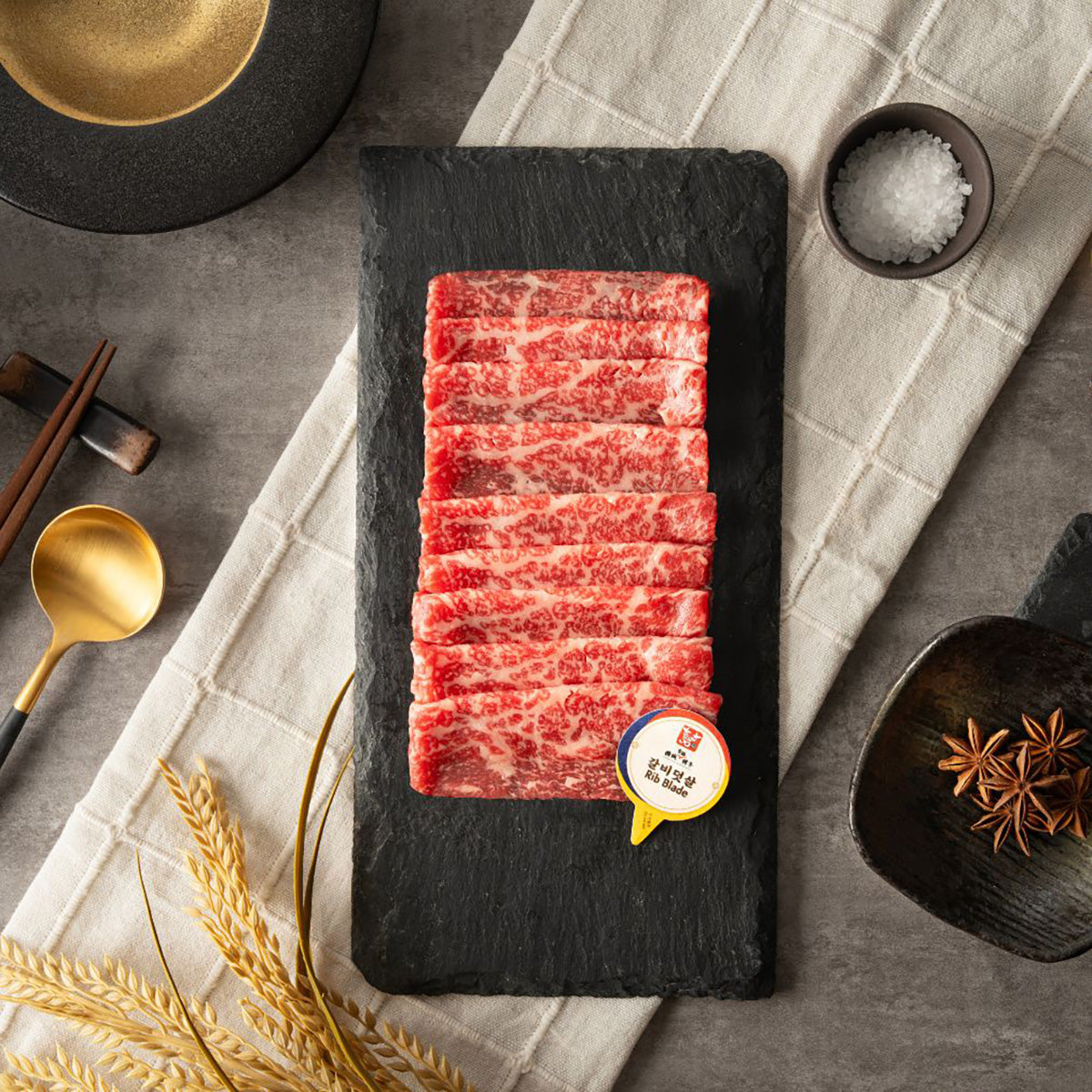 Chilled Hanwoo beef rib blade on black slate with marbled red slice stack