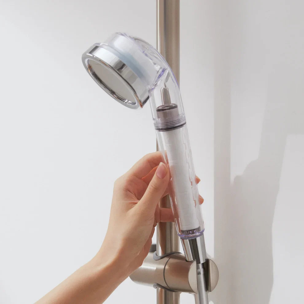 Chrome shower head with hand holding the shower handle near wall mount