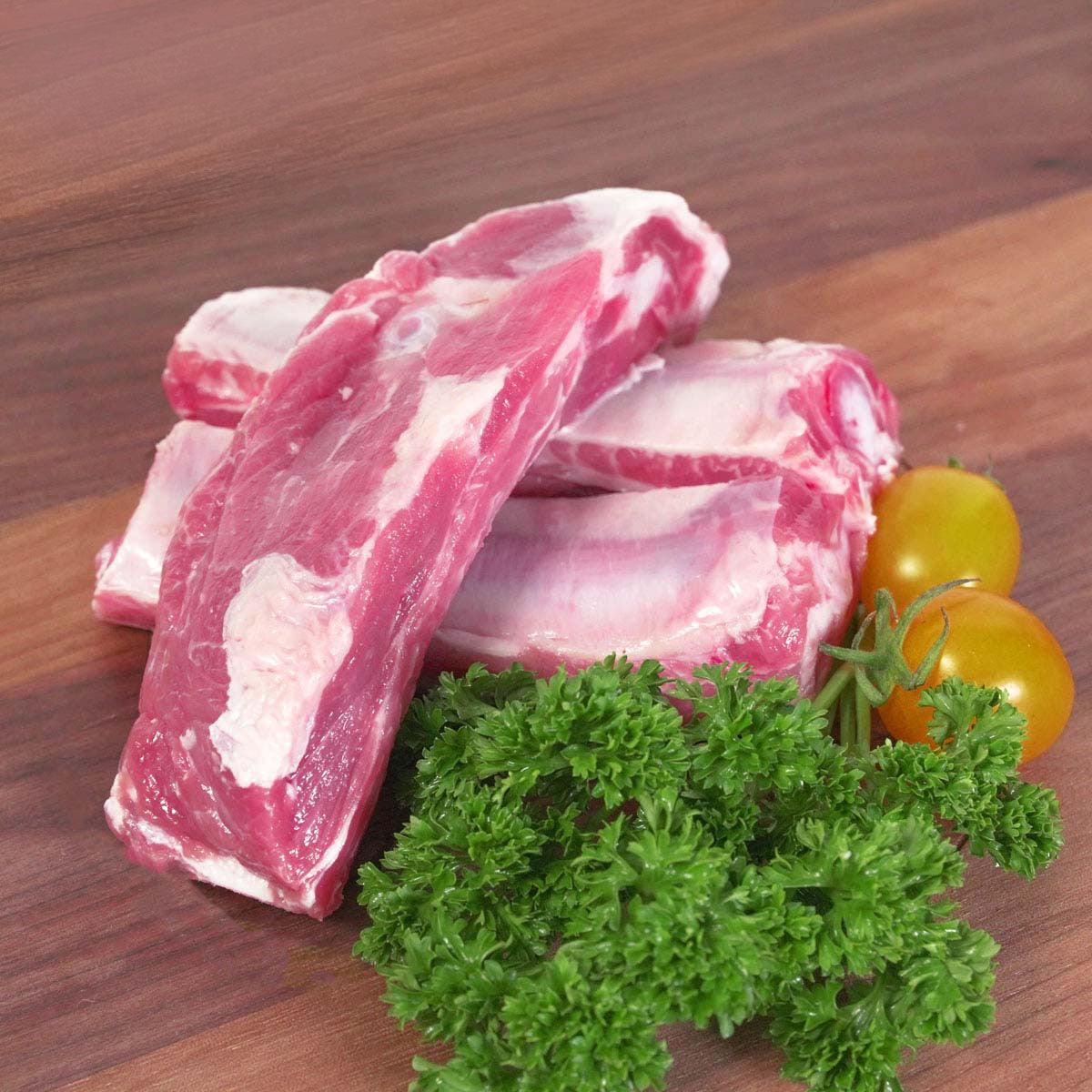 Frozen pork riblets with visible fat, garnished with parsley and cherry tomatoes